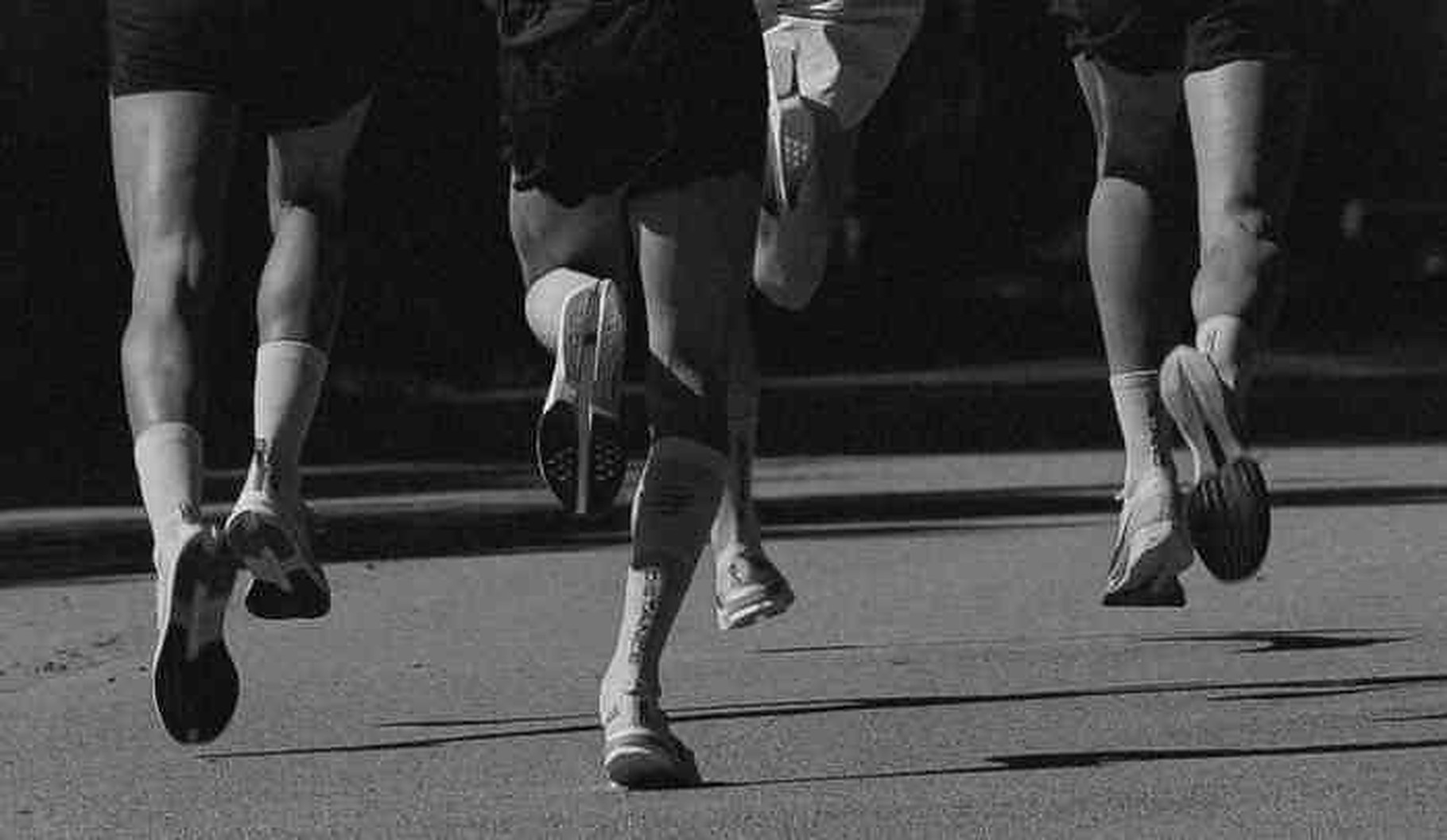 Piernas de tres corredores en plena zancada, en blanco y negro